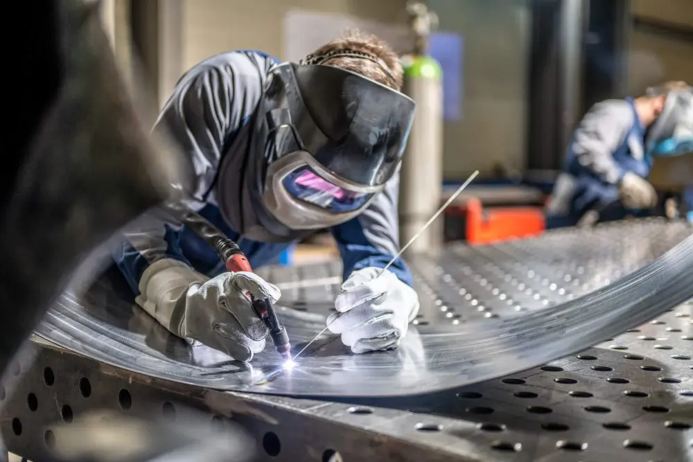 Soldadora masculina usando capacete trabalhando com maçarico de soldagem na fábrica.